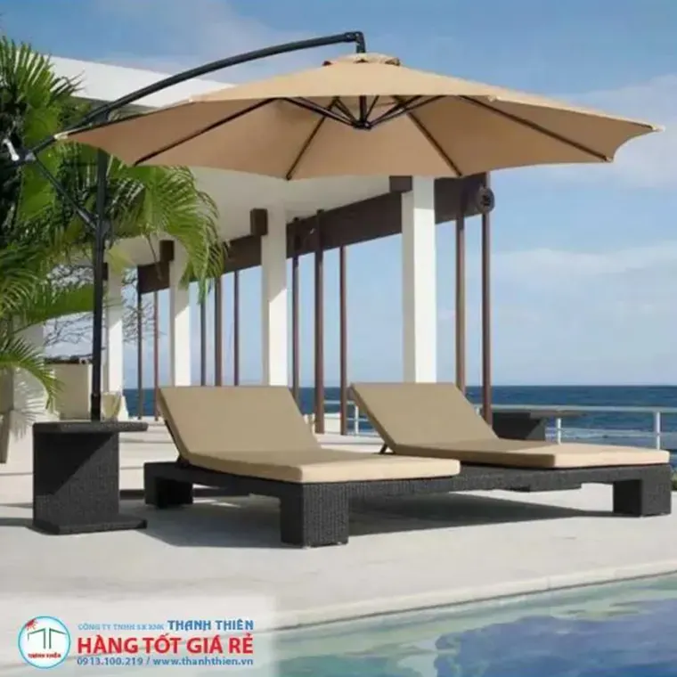Ô dù lệch tâm treo màu kem cạnh hồ bơi resort ven biển — ghế tắm nắng xếp đôi bên dưới tán không có cột cản