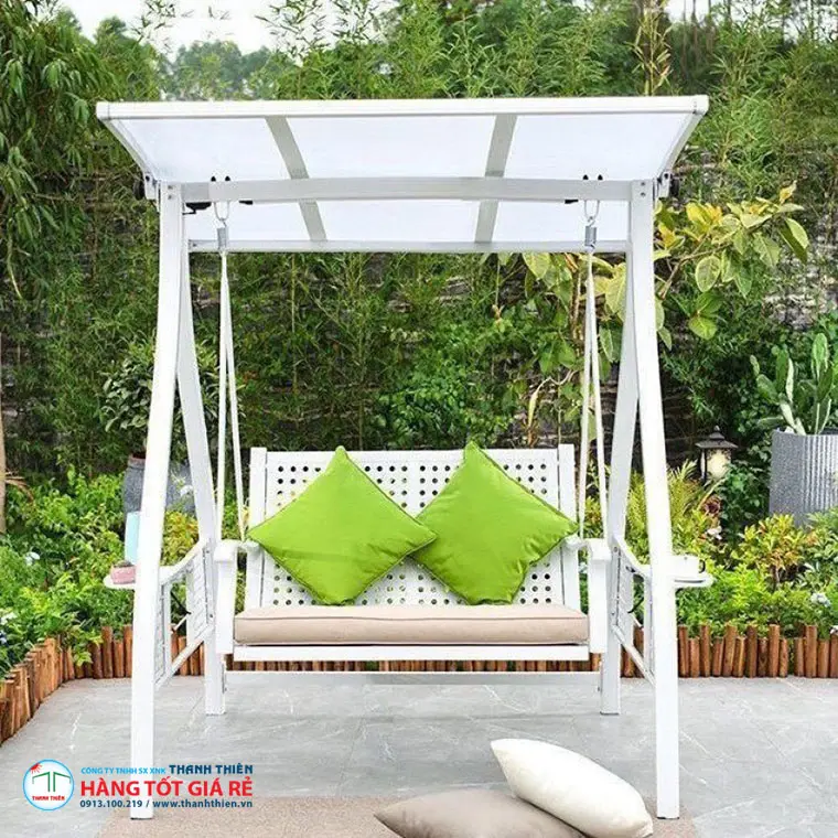 Ghế xích đu ngoài trời khung nhôm trắng, gối xanh lá solution-dyed, đặt trong sân vườn xanh — minh họa độ bền màu UV nhiệt đới